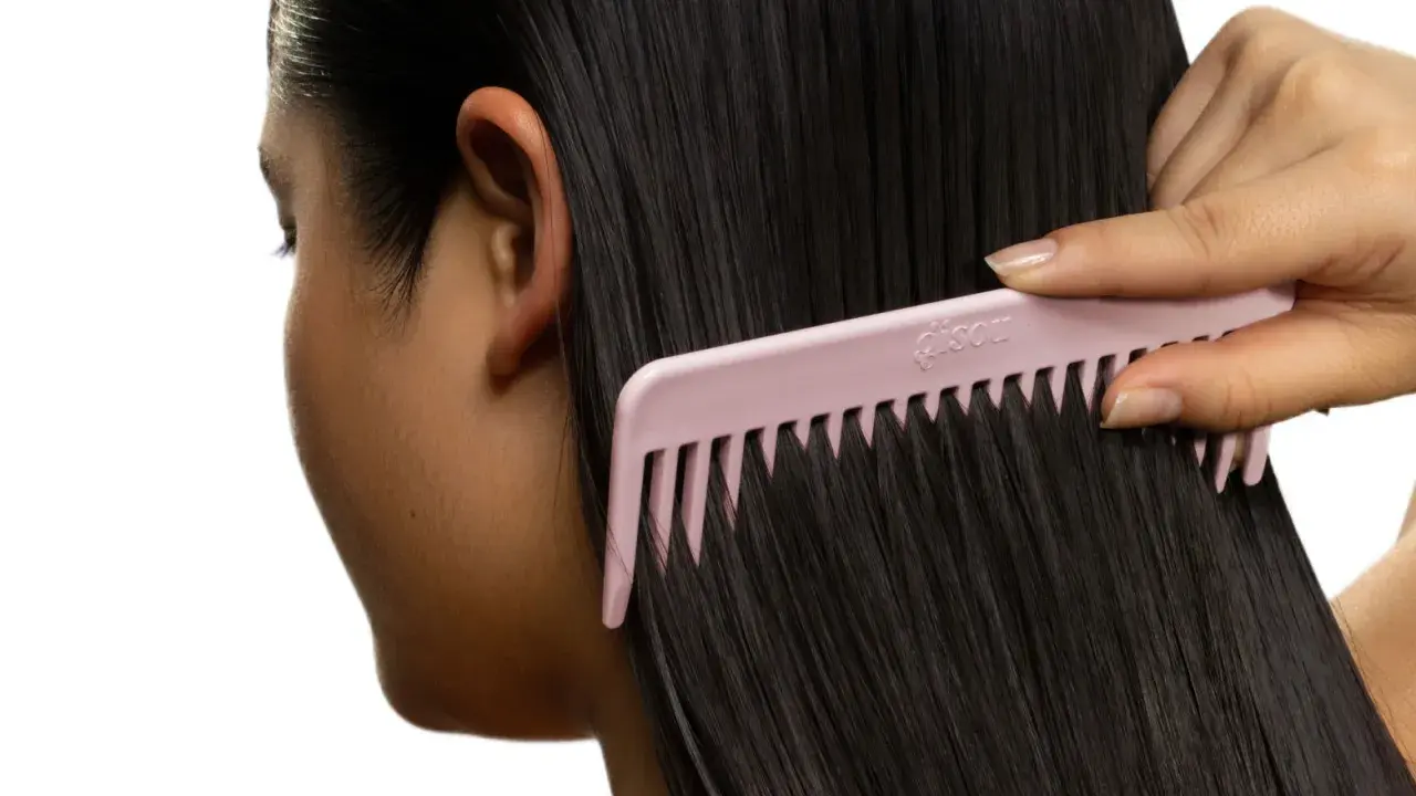 Une main peigne de longs cheveux noirs avec un peigne rose. Pas de nœud dans les cheveux, juste une chevelure soyeuse.