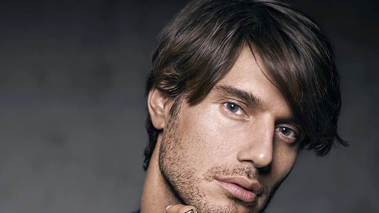 Un homme au regard intense, coiffé décoiffé, porte une bague ornée d'un motif discret.
