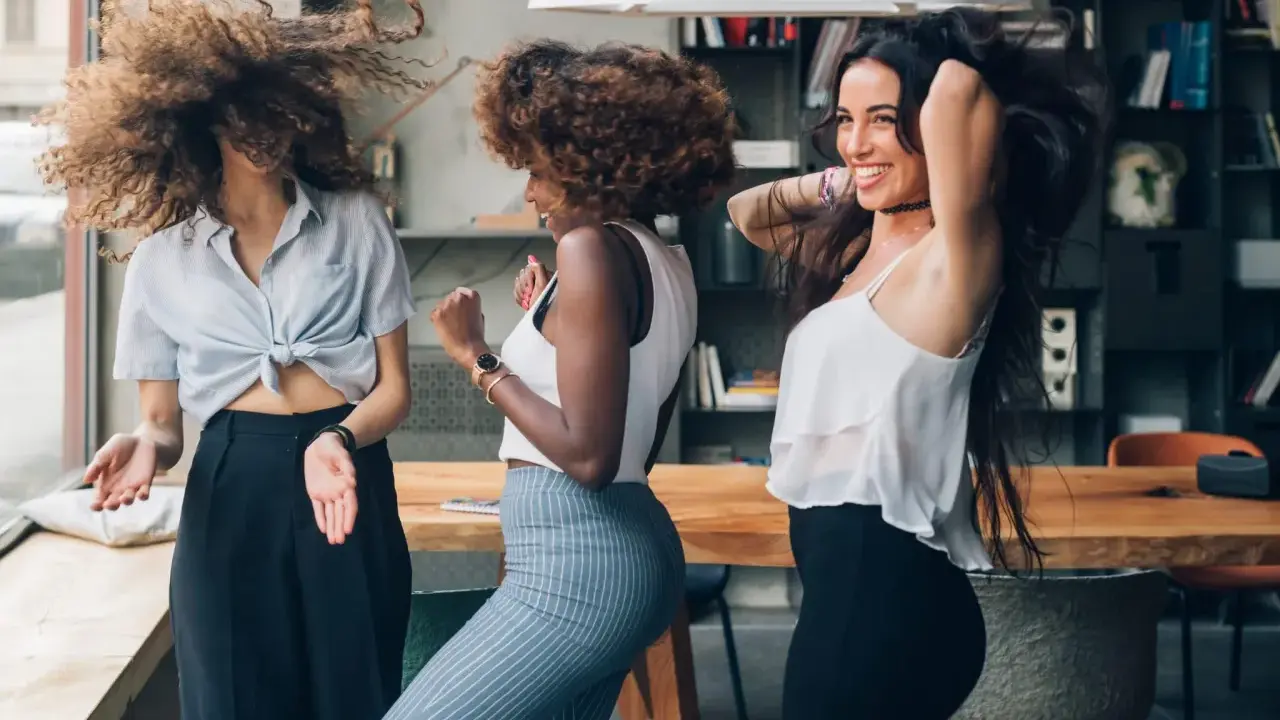 Trois femmes aux cheveux bouclés dansent joyeusement. Leurs chevelures volent, un exemple de comment avoir de belles boucles sans frisottis.