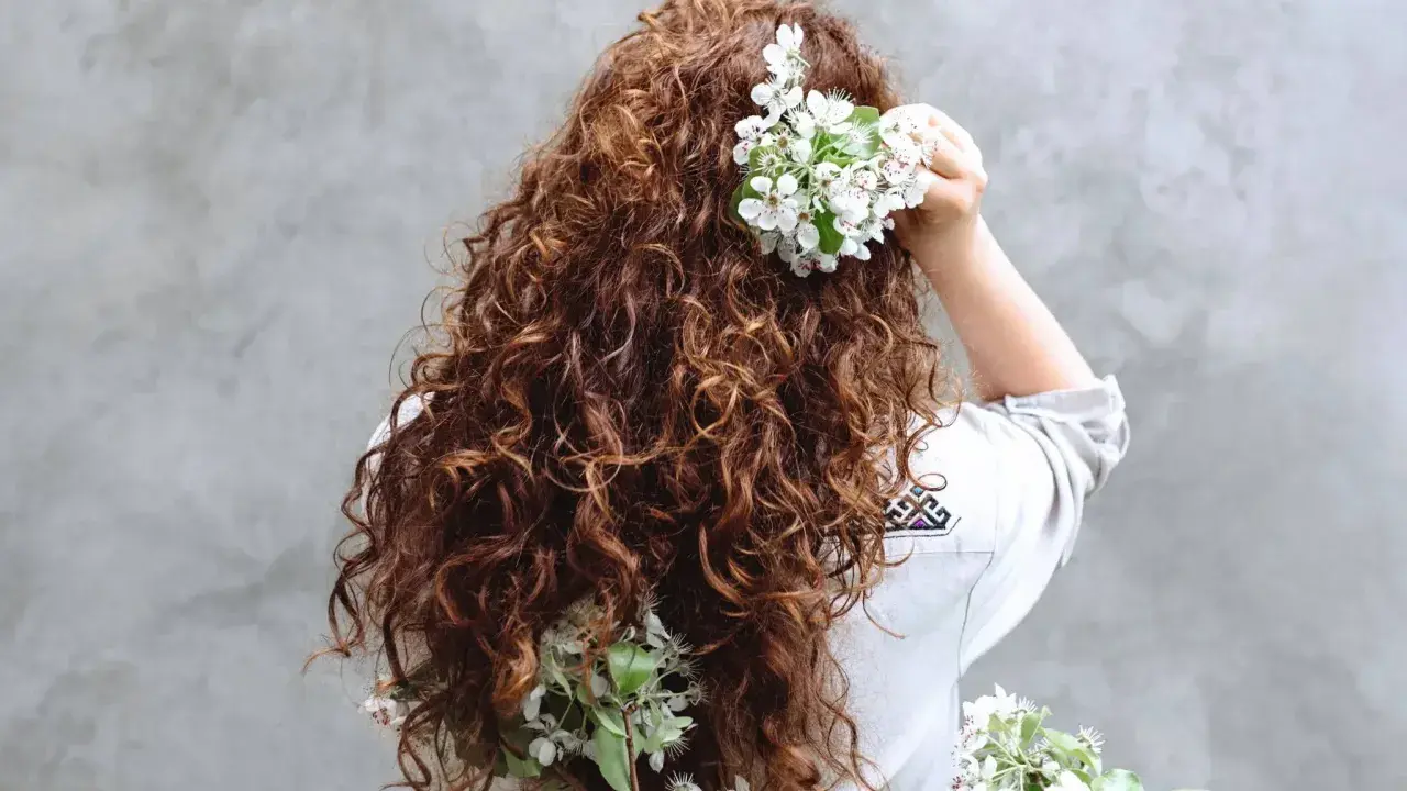 Chevelure brune et bouclée ornée de fleurs blanches, évoquant un décollement de racine naturel et printanier.