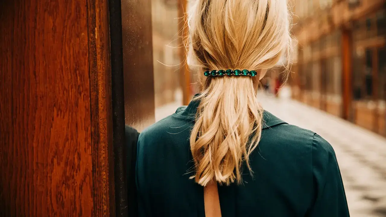 Coiffure avec barrette ornée de pierres vertes, retenant une queue de cheval blonde.