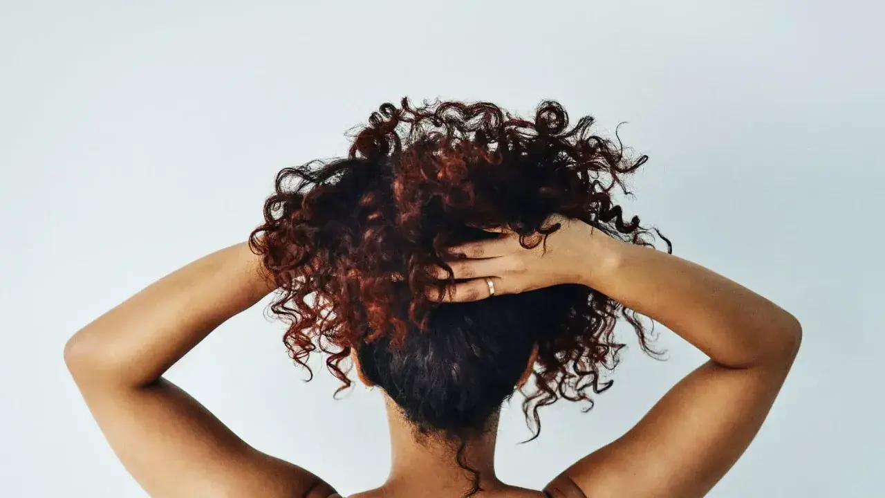 Cheveux bouclés, comme après une baignade dans l'eau salée, sont coiffés par des mains sur fond blanc.