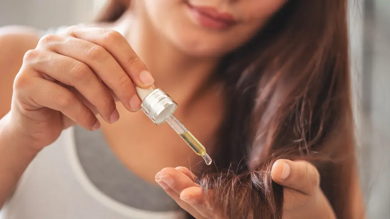 Une main applique une goutte d'huile sur la pointe des cheveux pour les nourrir.