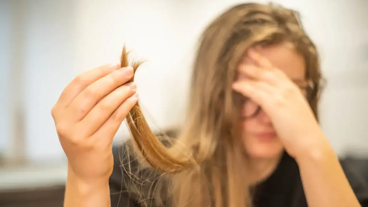 Une main tient une mèche de cheveux, visiblement abîmés, comme si c'était du cheveux mort. La personne semble désespérée.