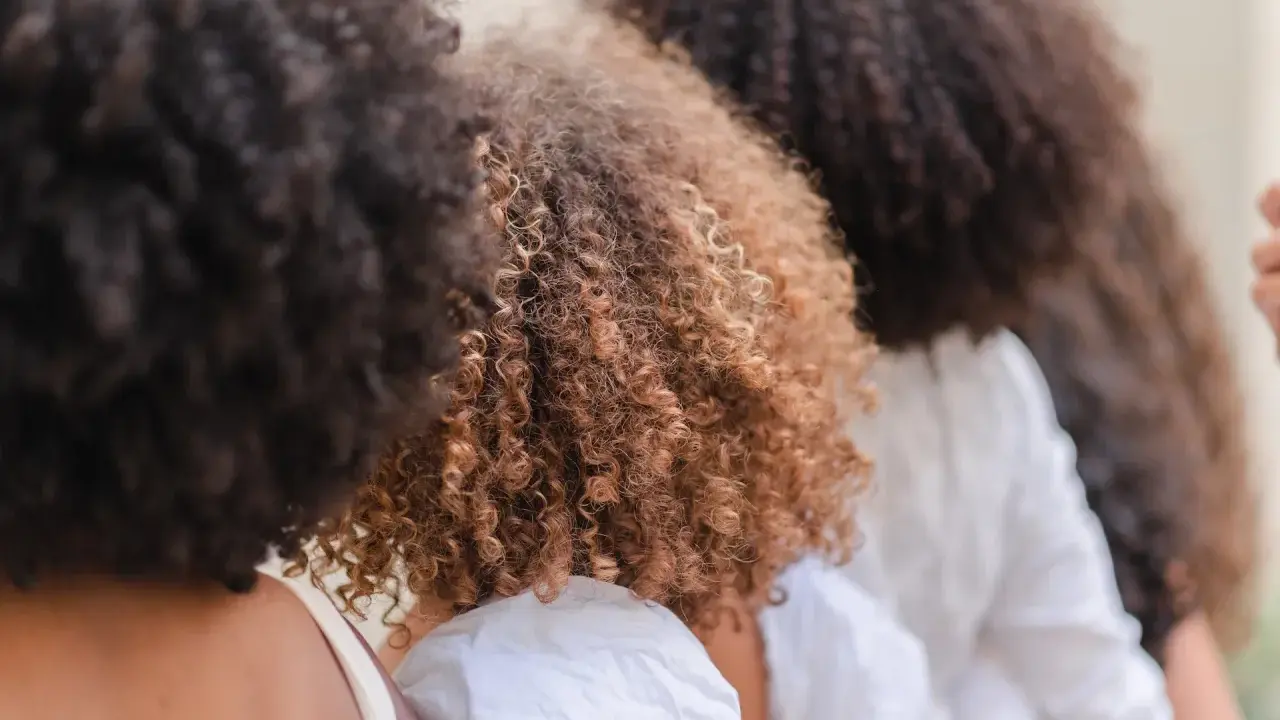 Trois femmes avec de magnifiques cheveux frisés, un mélange de bruns foncés et de châtain clair, se tiennent côte à côte.