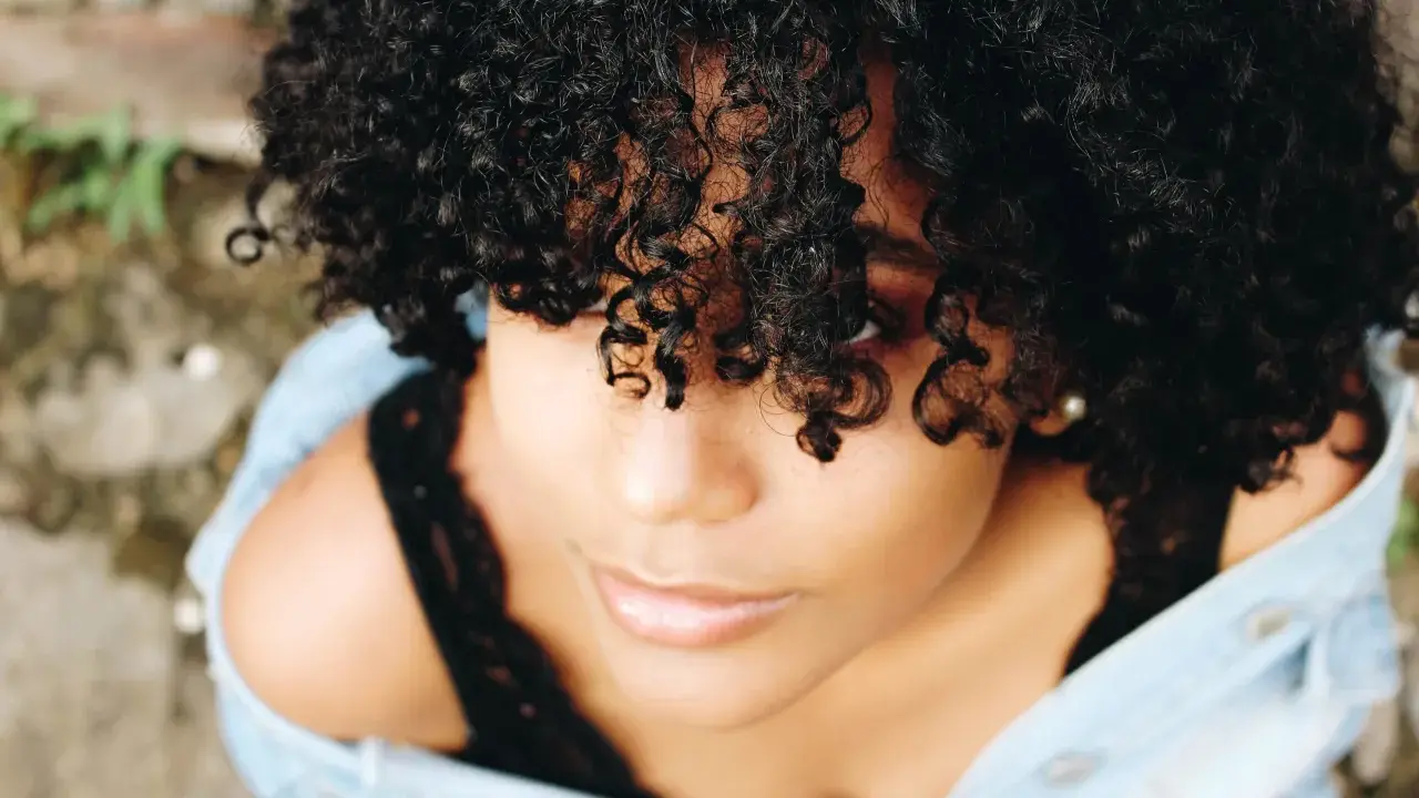 Une jeune femme aux cheveux bouclés naturels, une coiffure cheveux bouclés facile et magnifique, porte une veste en jean.