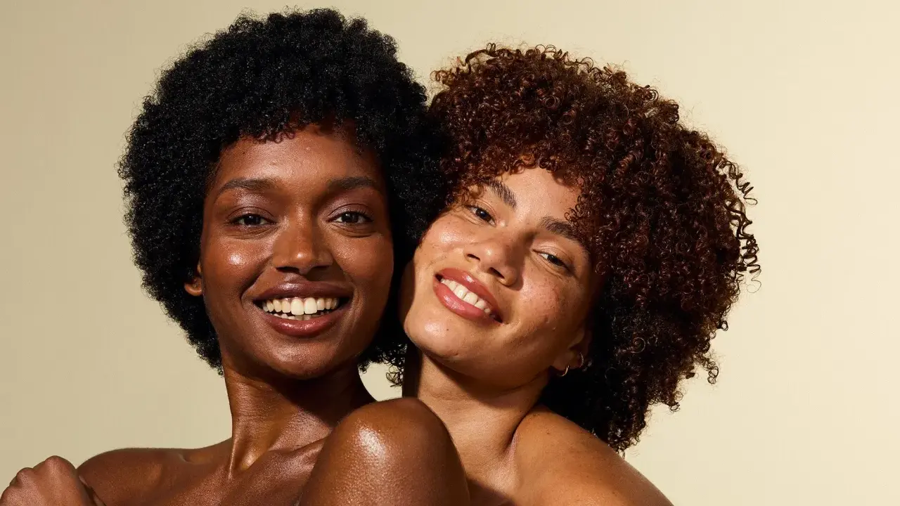 Deux femmes souriantes, l'une avec des cheveux crépus 4c noirs, l'autre avec des boucles rousses.
