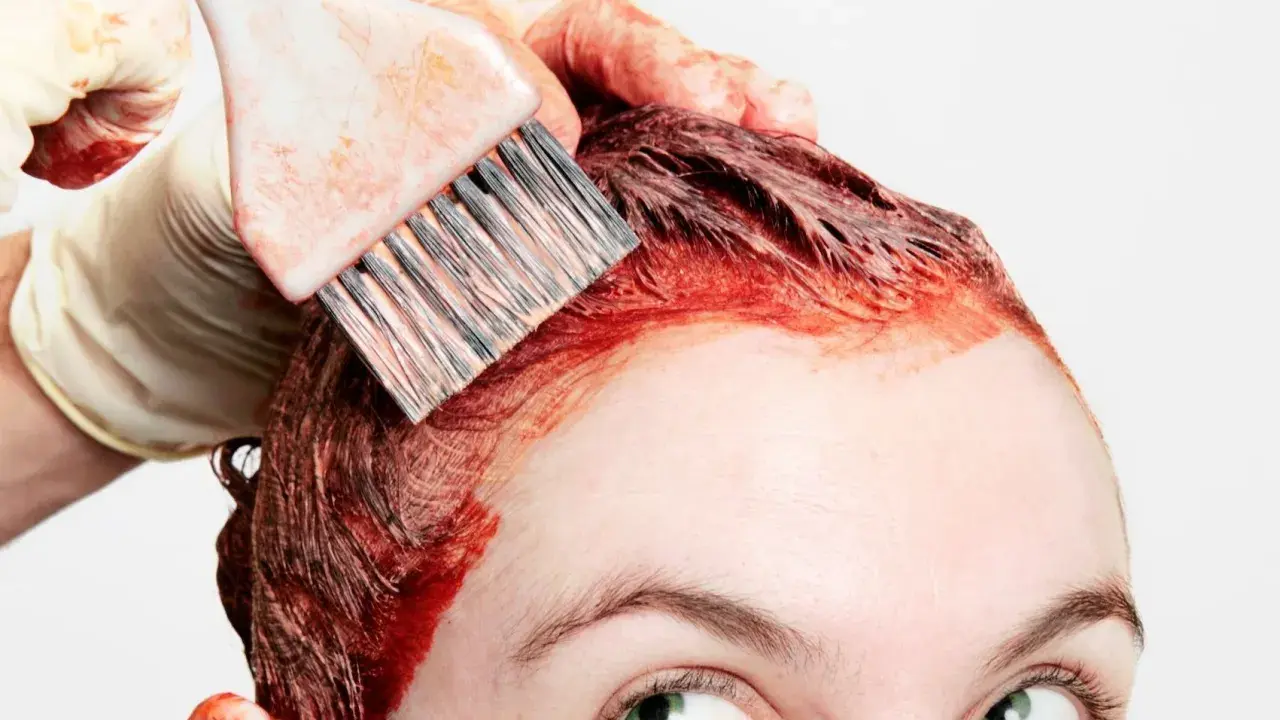 Application de teinture rouge sur les cheveux, étape clé de la routine cheveux colorés. Une main gantée utilise un pinceau pour une application précise.