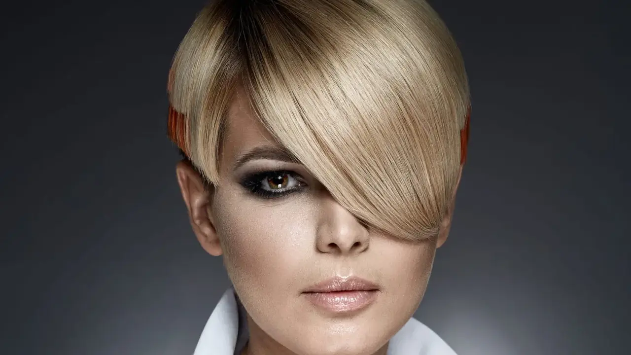 Une femme au regard intense arbore une coupe au bol audacieuse, avec des mèches blondes et des pointes orangées.
