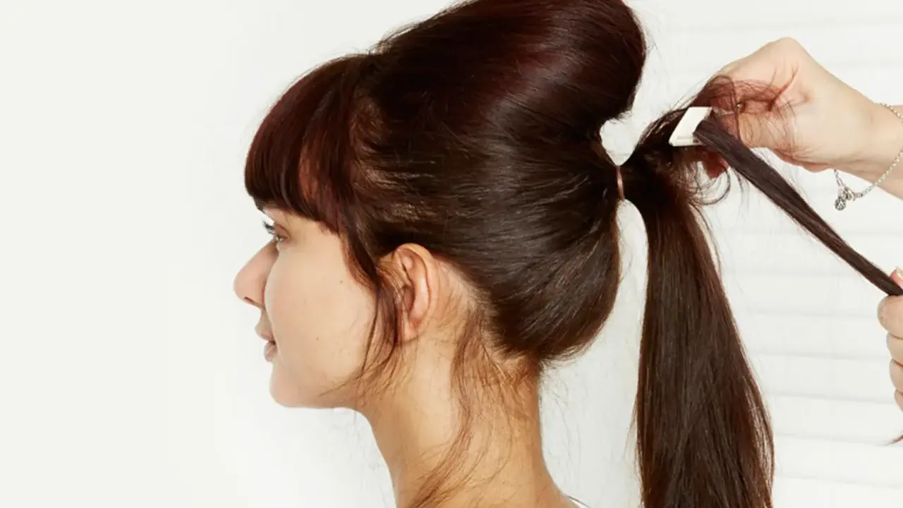 Une main ajuste une mèche pour créer un chignon sophistiqué. La coiffure volumineuse est en cours de réalisation.