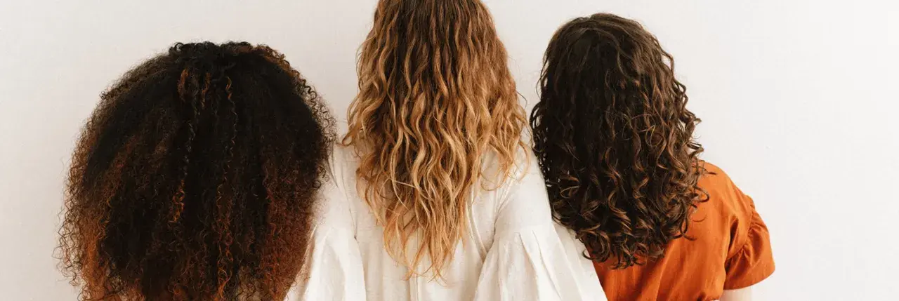 Trois femmes montrent leurs cheveux bouclés abîmés, de différentes couleurs et textures, sur fond blanc.