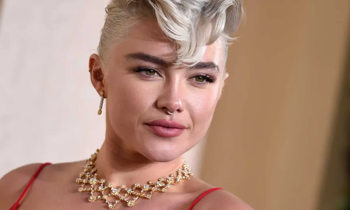 Une femme arbore une coupe courte blonde tendance, ornée d'un collier scintillant et d'une robe rouge.