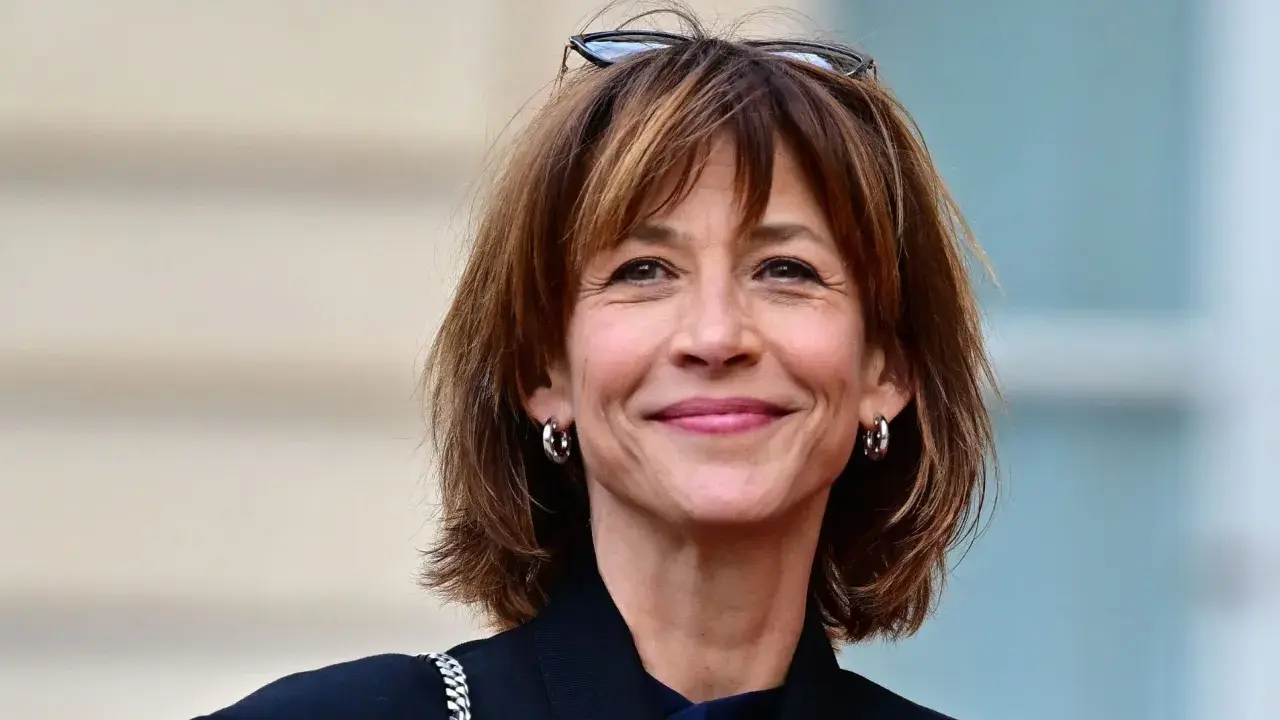 Une femme au sourire radieux arbore une coupe courte femme tendance, des lunettes sur la tête et des créoles argentées.