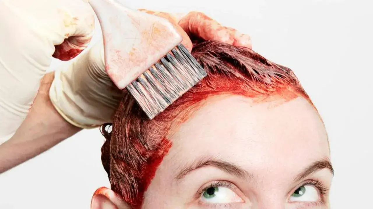 Application d'une teinture rouge pour un nouvel effet couleur cheveux. Une main gantée utilise un pinceau pour colorer les racines.
