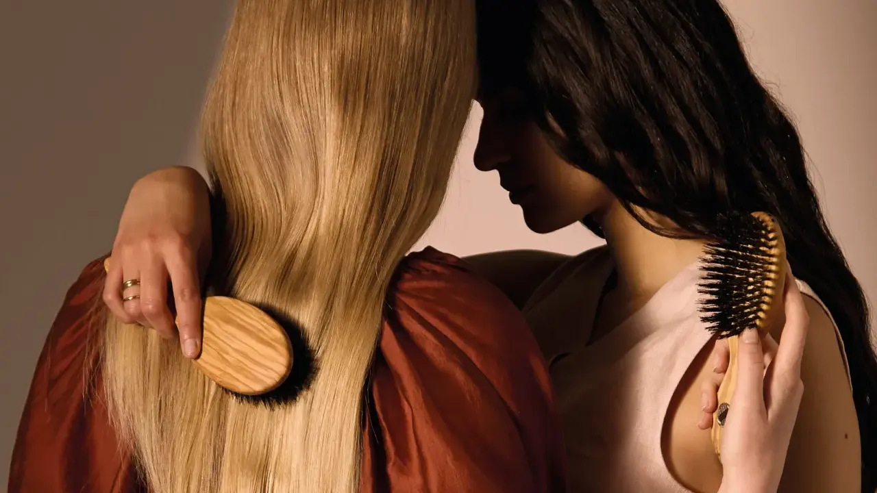 Deux femmes se serrent, l'une brosse les cheveux blonds de l'autre avec une brosse en bois.