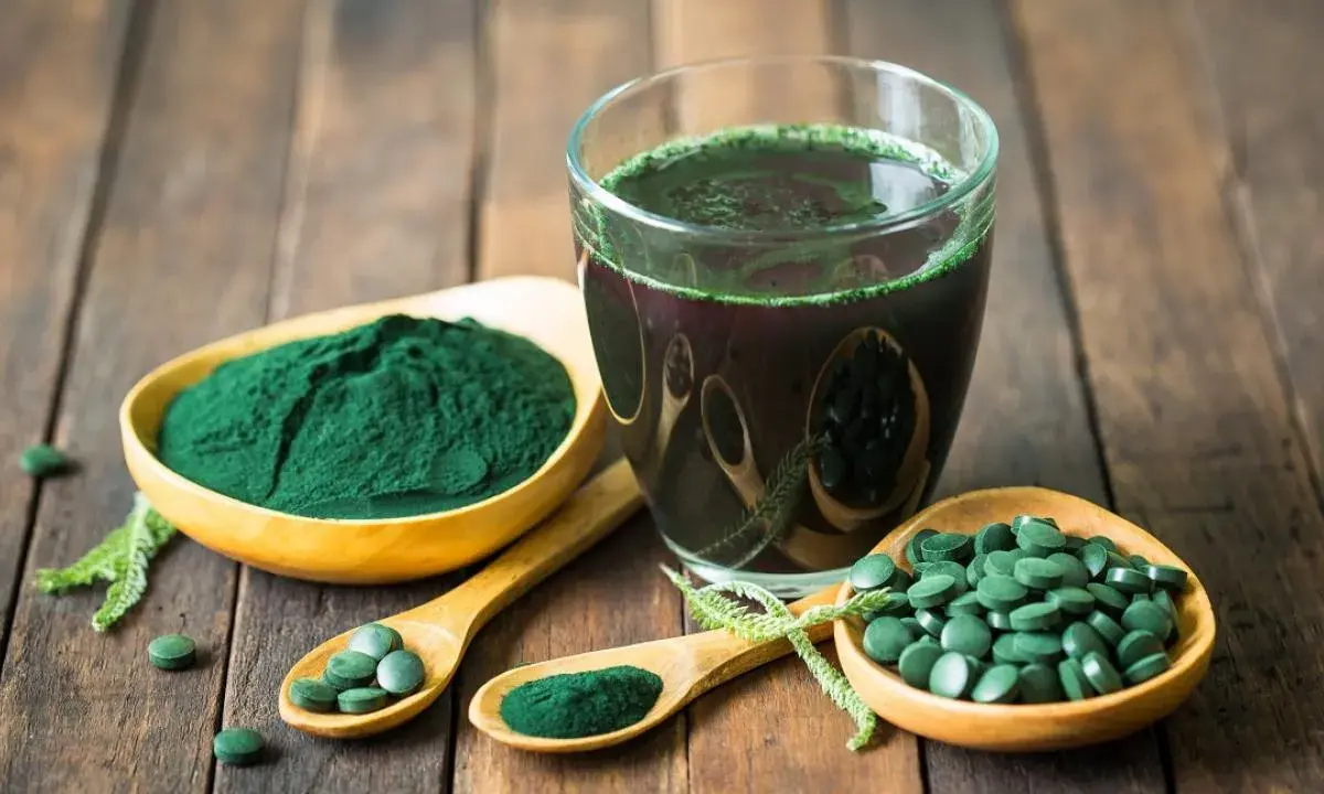 Spiruline en poudre, comprimés et boisson verte sur fond de bois. Découvrez les bienfaits spiruline cheveux pour une chevelure éclatante.