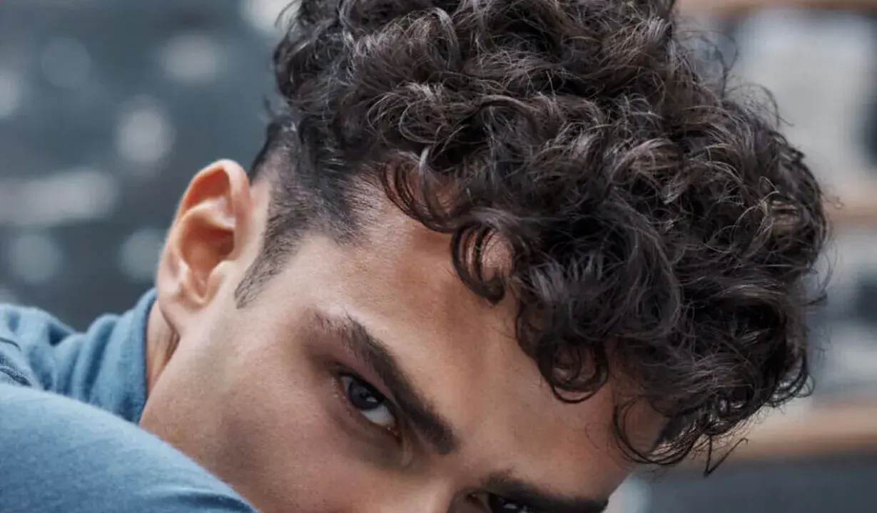 Gros plan sur un homme avec une coupe homme mi long bouclé, ses boucles sombres encadrant son visage.