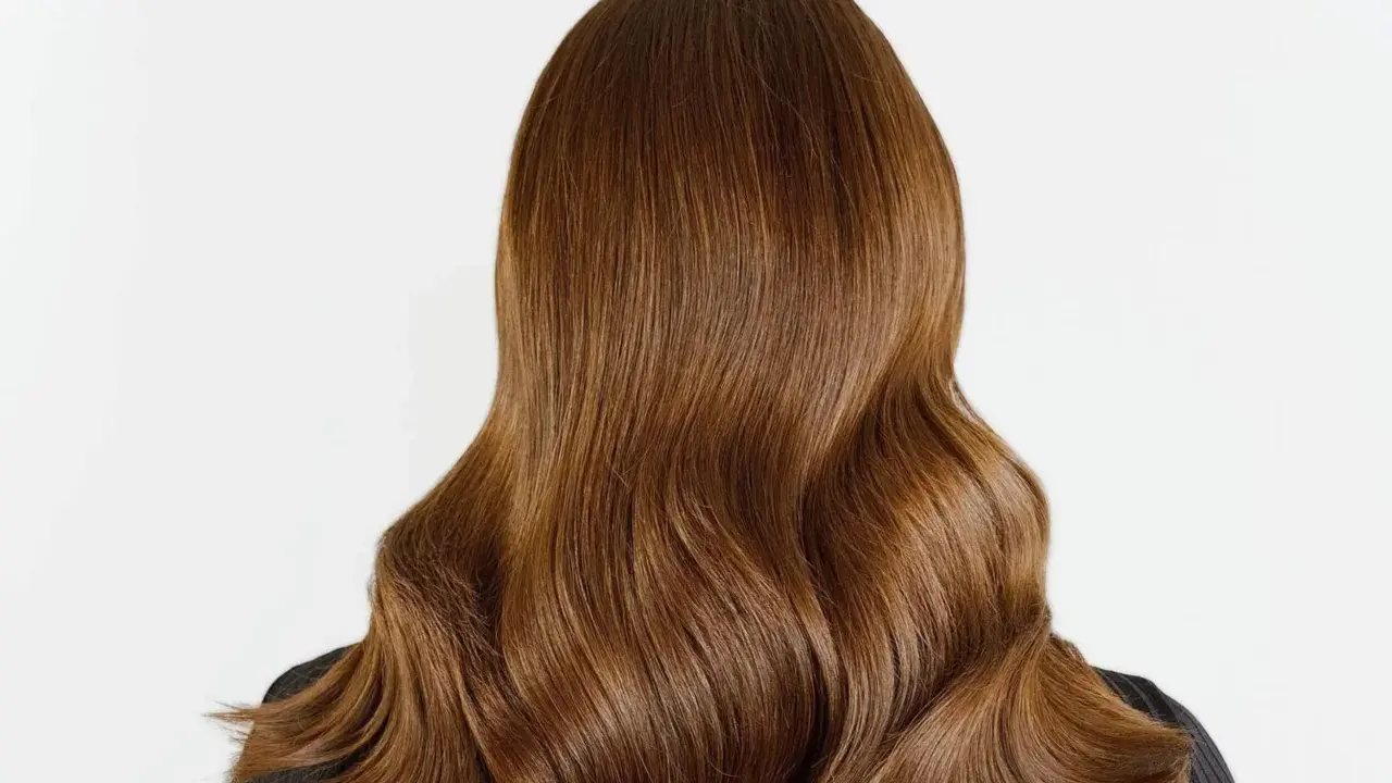 Chevelure brune aux reflets chauds, un balayage chatain clair subtil illumine ces ondulations douces.