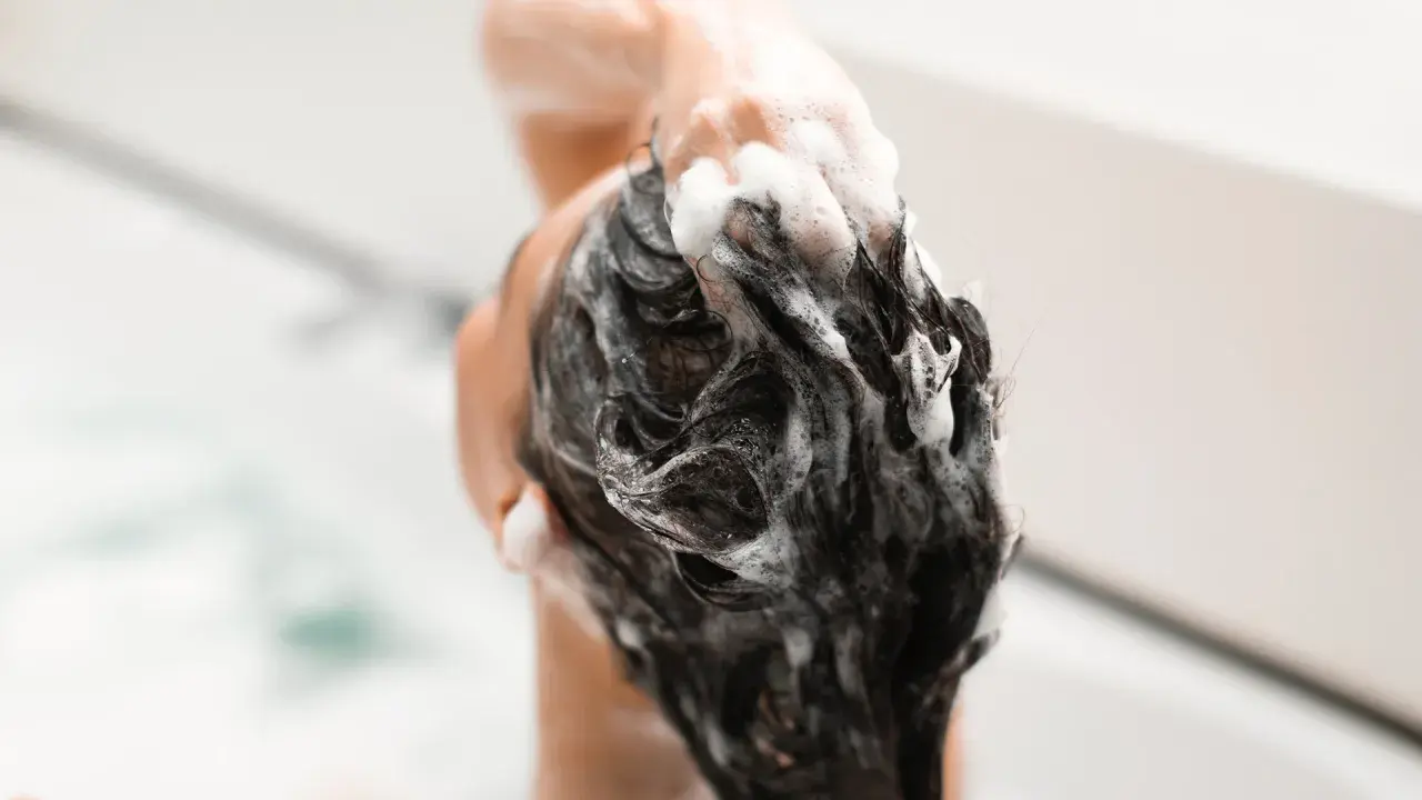 Mousse de shampoing sans silicone, une main masse le cuir chevelu sous une douche.