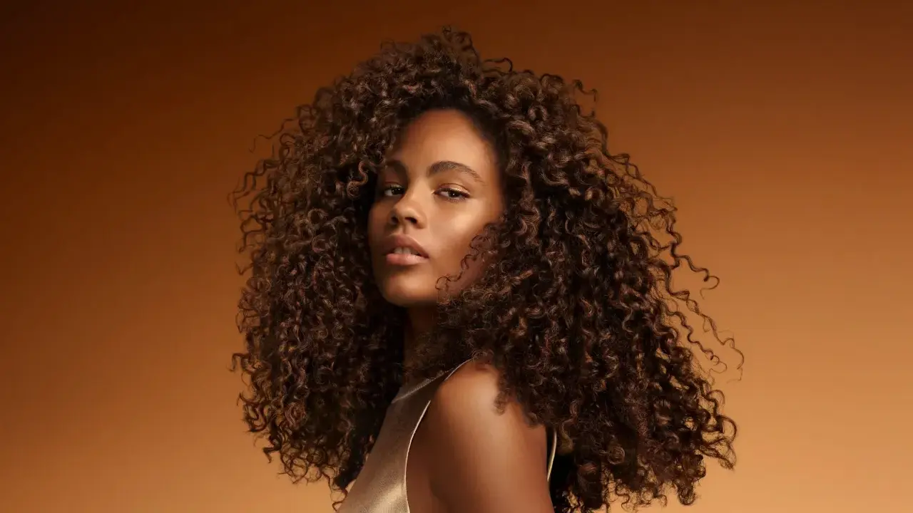 Une jeune femme aux cheveux bouclés et brillants, un exemple de comment bien rincer ses cheveux pour un éclat naturel.