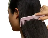 Une main peigne de longs cheveux noirs avec un peigne rose. Pas de nœud dans les cheveux, juste une chevelure soyeuse.