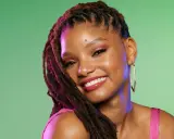 Jeune femme souriante avec une coiffure avec bijoux cheveux, des dreadlocks ornées de reflets violets, et de grandes boucles d'oreilles dorées.