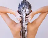 Dos mains appliquent un masque capillaire sur des cheveux longs et bruns. Attention à ne pas laisser poser un masque cheveux trop longtemps !