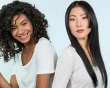 Deux femmes souriantes, l'une aux cheveux bouclés, l'autre aux cheveux lisses. La première joue avec ses mèches, évitant les cheveux fourchus jusqu'à la racine.