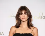 Une jeune femme au regard intense, arborant une **frange rideaux courte** et une robe noire. Le logo OMEGA est visible en arrière-plan.