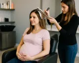 Une femme enceinte profite d'un balayage chez le coiffeur. Elle tient son ventre avec un sourire doux.