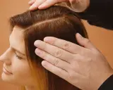 Mains caressant des cheveux châtains, séparés en deux sections. Une femme regarde vers le bas, l'air pensif, peut-être à cause de ses cheveux moches.