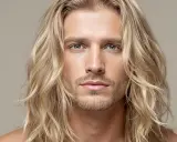 Un homme aux longs cheveux blonds ondulés, un regard intense et une barbe naissante. Sa mèche blonde encadre son visage.