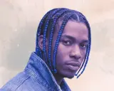 Un jeune homme aux tresses bleues éclatantes, portant une veste en jean, pose avec confiance.