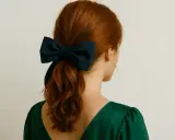 Une queue de cheval aux cheveux roux est ornée d'un grand nœud bleu marine, ajoutant une touche d'élégance à cette coiffure.