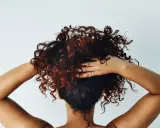 Cheveux bouclés, comme après une baignade dans l'eau salée, sont coiffés par des mains sur fond blanc.