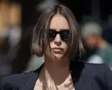 Une femme au regard intense arbore une coupe carré droit dégradé, accentuée par des lunettes de soleil noires et un blazer chic.