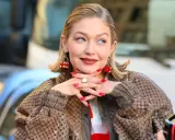 Gigi Hadid, avec ses boucles d'oreilles en forme de dé rouge, pose avec un sourire malicieux. Son carré plaqué en arrière et son manteau texturé complètent son look.