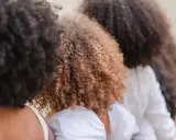Trois femmes avec de magnifiques cheveux frisés, un mélange de bruns foncés et de châtain clair, se tiennent côte à côte.