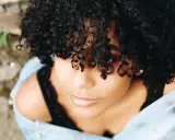 Une jeune femme aux cheveux bouclés naturels, une coiffure cheveux bouclés facile et magnifique, porte une veste en jean.