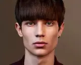 Un jeune homme au regard intense arbore une coupe au bol homme audacieuse, encadrant son visage aux traits fins.