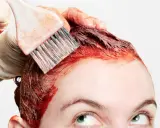 Application de teinture rouge sur les cheveux, étape clé de la routine cheveux colorés. Une main gantée utilise un pinceau pour une application précise.