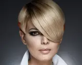 Une femme au regard intense arbore une coupe au bol audacieuse, avec des mèches blondes et des pointes orangées.