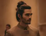 Un homme au man bun élégant, portant une veste texturée, pose avec assurance.