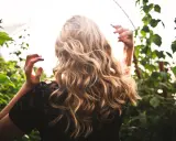 Chevelure blonde ondulée, baignée de lumière, entourée de verdure. Une scène évoquant la douceur d'une **décoloration végétale** naturelle.