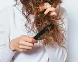 Une personne démêle ses cheveux mouillés et **cheveux emmêlés à la racine** avec un peigne noir.