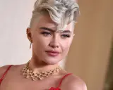 Une femme arbore une coupe courte blonde tendance, ornée d'un collier scintillant et d'une robe rouge.