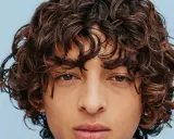 Un jeune homme au regard intense arbore une magnifique coupe cheveux bouclés homme, des boucles brunes et rebelles encadrant son visage.
