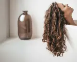 Une femme aux cheveux bouclés se détend dans une baignoire. Elle se demande combien de shampoing par lavage est idéal pour ses cheveux.