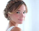 Une jeune femme au sourire doux arbore une coiffure demi tresse élégante, ses cheveux blonds ornés d'une tresse subtile.