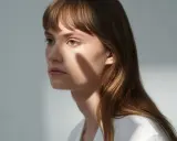 Une jeune femme aux cheveux châtains, une ombre sur le visage, parfaite pour apprendre comment coiffer une frange sur le côté.